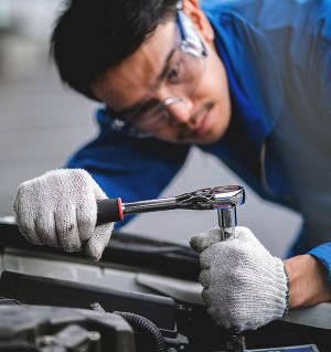 A man in a blue shirt and white gloves is working on a car. He is using a wrench to loosen a bolt